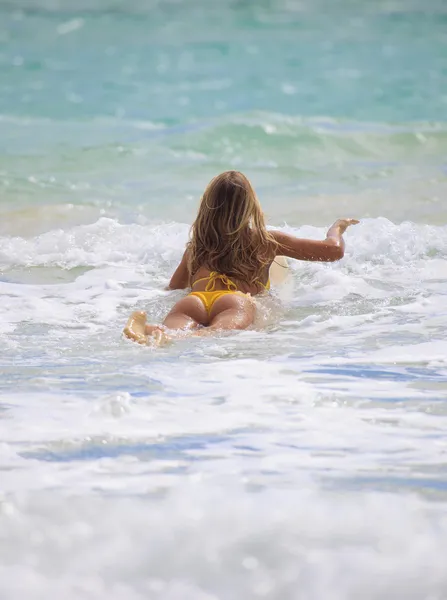 在比基尼的金发女孩桨她的冲浪板 — 图库照片