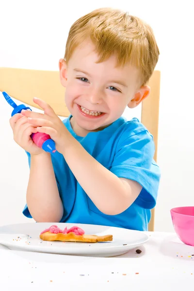 Boy decorating baked biscuits — Stock Photo, Image