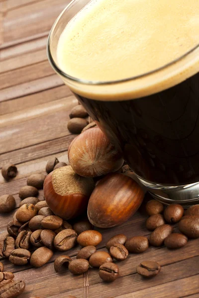 Kaffebönor och hasselnötter nära espresso i en kort glas kopp — Stockfoto