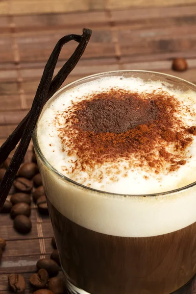 Coffee with milk froth, cocoa powder and standing vanilla beans — Stock Photo, Image