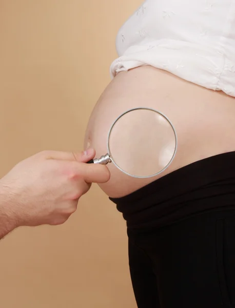 Looking pregnant belly with magnifying glass — Stock Photo, Image