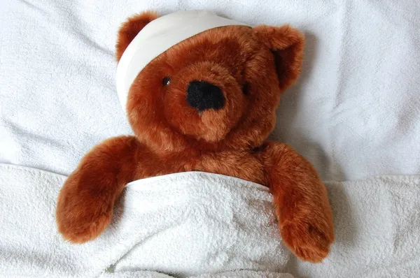 Sick teddy with injury in bed Stock Image