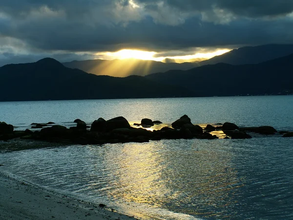 Solen strålar igenom moln över mountais och reflektion på ocea — Stockfoto