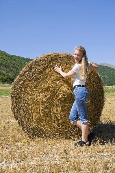 stock image Blonde girl leaning against a rolling haystack.