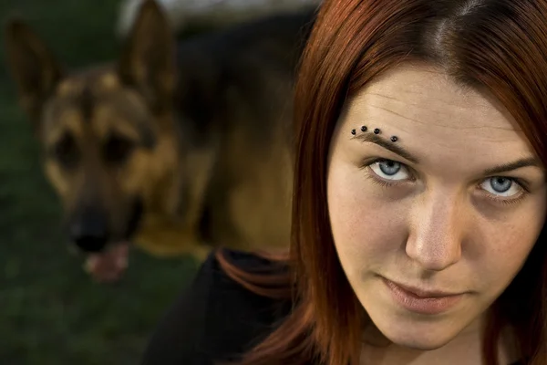 A lány nézi a kamera a kutyájával, a háttérben — Stock Fotó