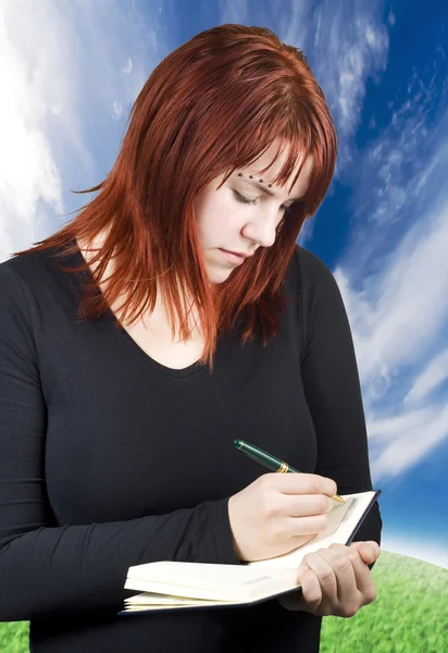 Cute redhead writing in her notebook or diary — Stock Photo, Image