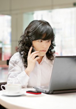 Woman using a laptop computer and phone clipart