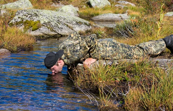 Člověk pije vodu z potoka — Stock fotografie