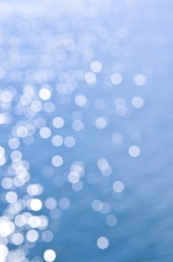 Out of focus bokeh background of blue water with sun reflections clipart