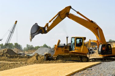 Yellow bulldozer machines digging and moving earth at construction site clipart