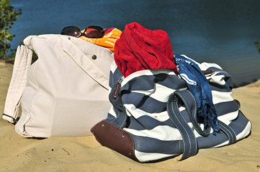 Summer beach bags on sand with towels and sunglasses clipart