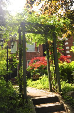 Landscaped front yard of a house with flowering garden and arbor. Lens flare is intentional. clipart