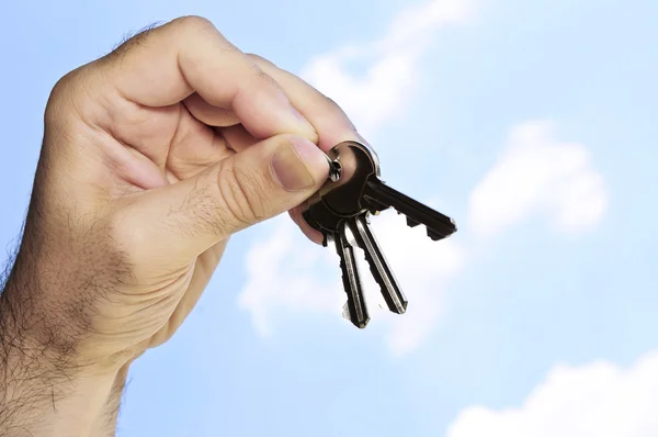 男人的手拿着房门钥匙 在蓝蓝的天空背景上 — 图库照片
