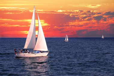 Sailboat sailing on a calm evening with dramatic sunset clipart
