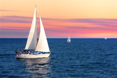 Sailboat sailing towards sunset on a calm evening clipart