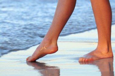 Feet of a young woman trying water on tropical beach clipart