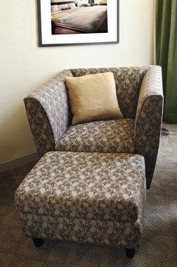 Comfortable armchair with cushion and ottoman. Photo on the wall is my own. clipart