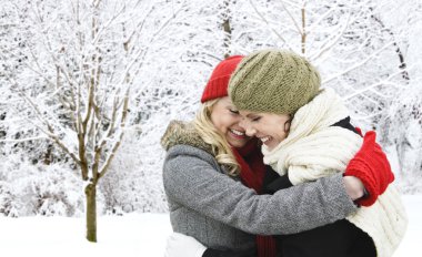 Two girl friends hugging outside in winter clipart