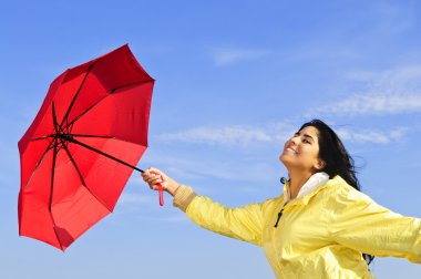 Portrait of beautiful girl wearing yellow raincoat holding red umbrella on windy day clipart