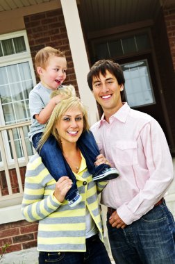 Young happy family standing in front of new home clipart