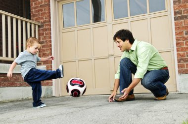 Father teaching son to play soccer on driveway clipart