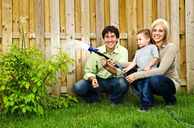 Happy family in backyard watering plant with hose clipart