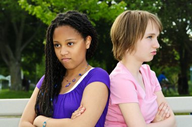 Two unhappy teenage girls sitting on bench clipart