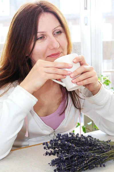 リラックスの成熟した女性は自宅でカップを置く — ストック写真