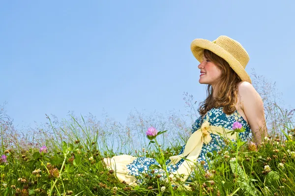 麦わら帽子で夏の草原の上に座って若い 代の少女 — ストック写真