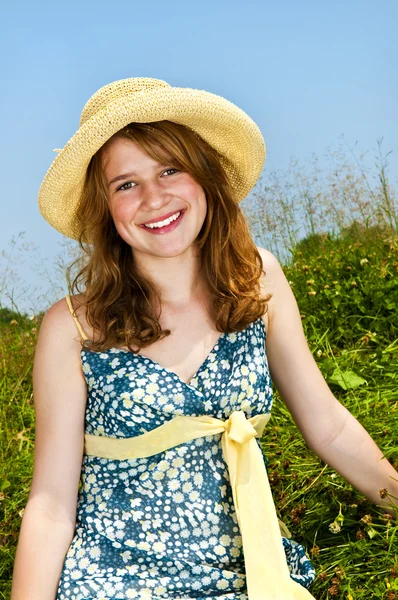 麦わら帽子で夏の草原の上に座って若い 代の少女 — ストック写真