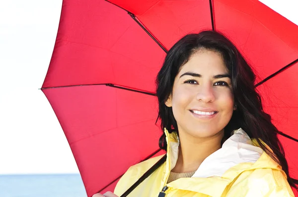 身穿黄色雨衣持红伞的美丽微笑着黑发女孩的肖像 — 图库照片