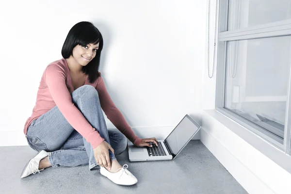 笑みを浮かべて床に座っているラップトップ コンピューターで若い黒人女性 — ストック写真