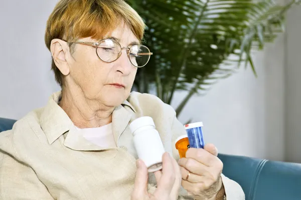 高齢者の女性が薬で薬瓶に警告表示を読む — ストック写真