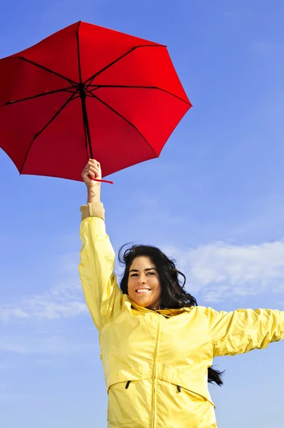 美丽的女孩穿着黄色雨衣上刮风的日子举行红伞的肖像 图库图片