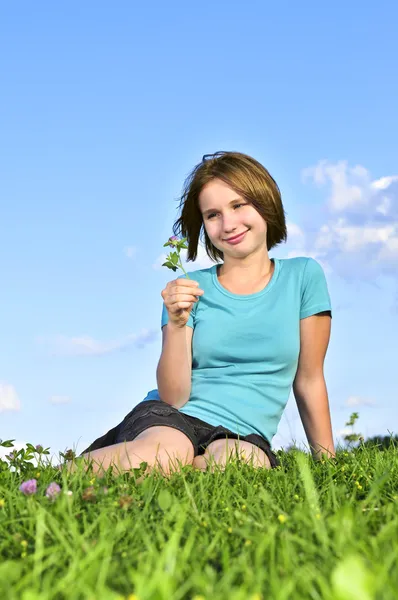 年轻的少女坐在草地上和嗅到一朵花 — 图库照片