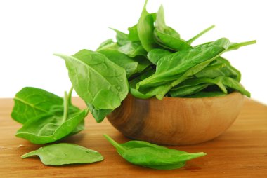 Fresh spinach iin a wooden bowl on a cutting board clipart