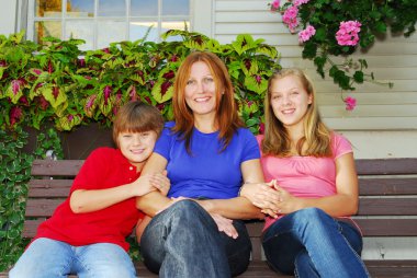 Family of mother and children sitting in front of their house clipart