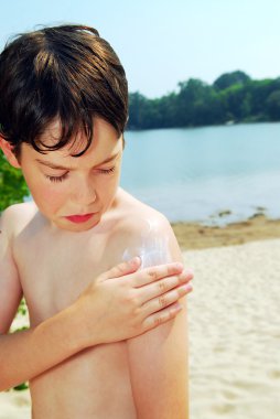 Young boy applying sunscreen on a beach clipart