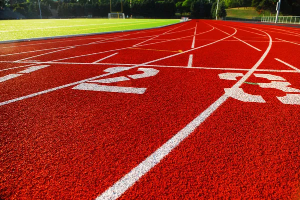 stock image Curving lanes of a red race track and green football field