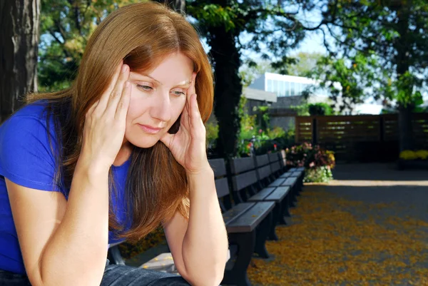 成熟的女人坐在公园的长凳上头痛 — 图库照片