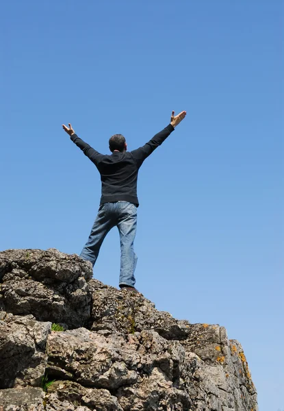 一个男人站在悬崖上用他的胳膊提高到蓝色的天空 — 图库照片