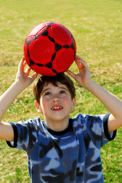 Χαριτωμένο Ευτυχείς Αγόρι Εξισορρόπηση Ένα Κόκκινο Ποδόσφαιρο Αγόρι Στο Κεφάλι — Φωτογραφία Αρχείου