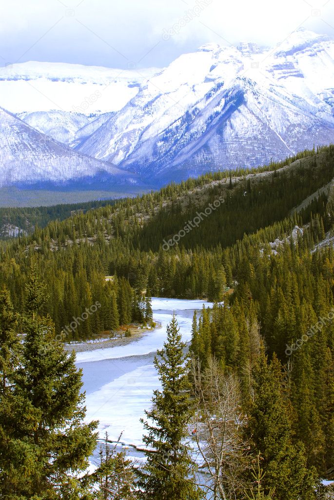 Landscape of high snowy mountains with evegreen trees and frozen river
