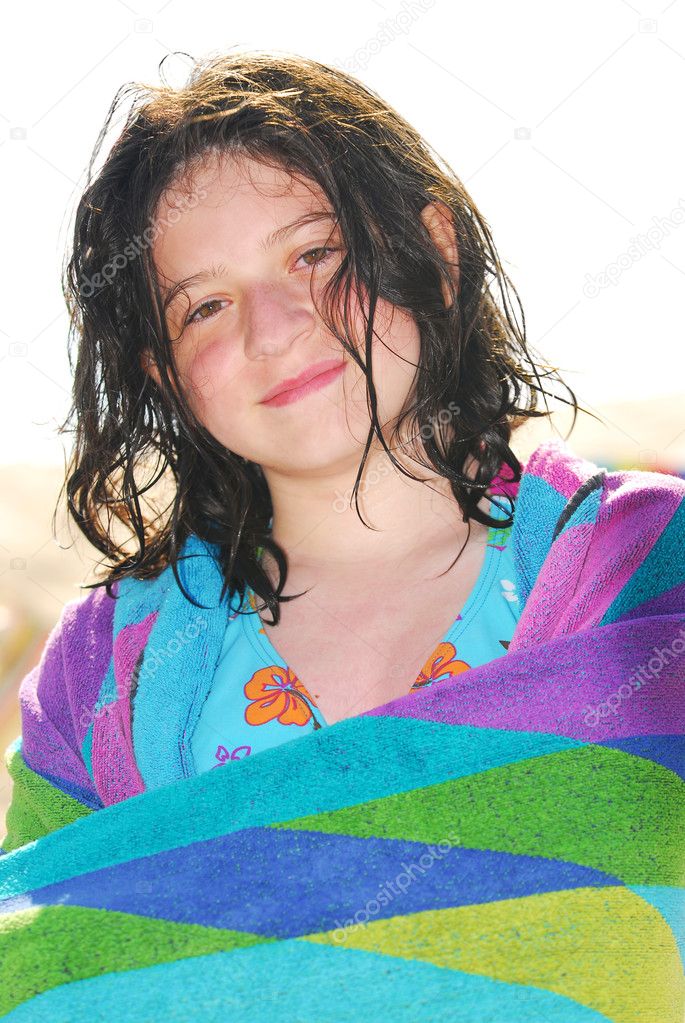 Young girl wrapped in a towel on a beach relaxing after swimming