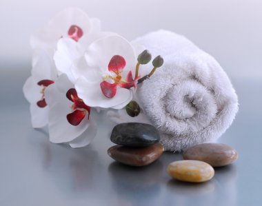 White rolled up towel with massage stones and an orchid clipart