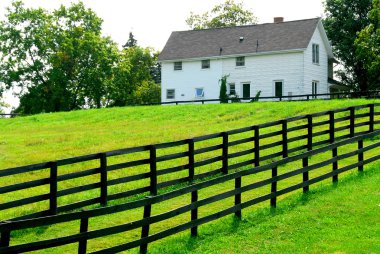 Farmhouse with fence among green fields clipart