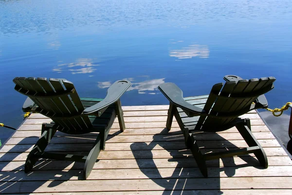 Two Adirondack Wooden Chairs Dock Facing Blue Lake Clouds Reflections — Stock Photo, Image