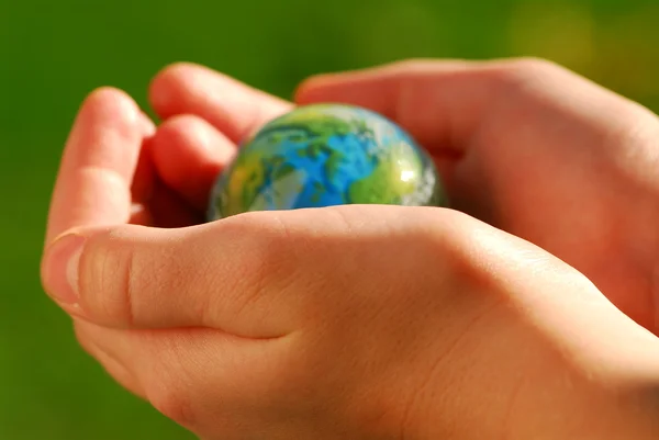緑の背景に地球を支えて子供の手 — ストック写真