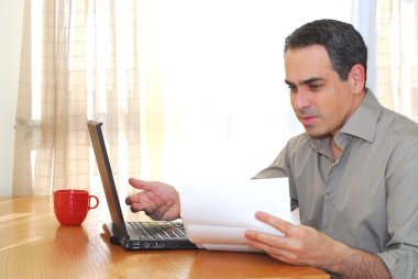 Man sitting at his desk with a laptop looking at bills clipart