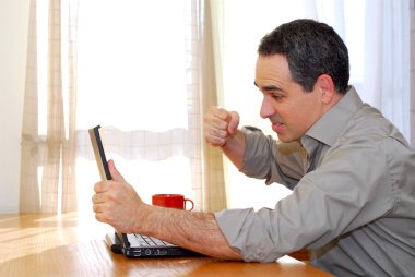 Man sitting at a desk punching his computer in frustration clipart